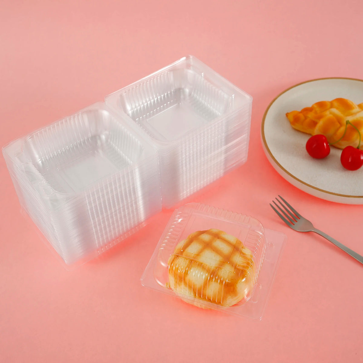 A clear plastic box with a lid containing a piece of glazed cake on a pink background.