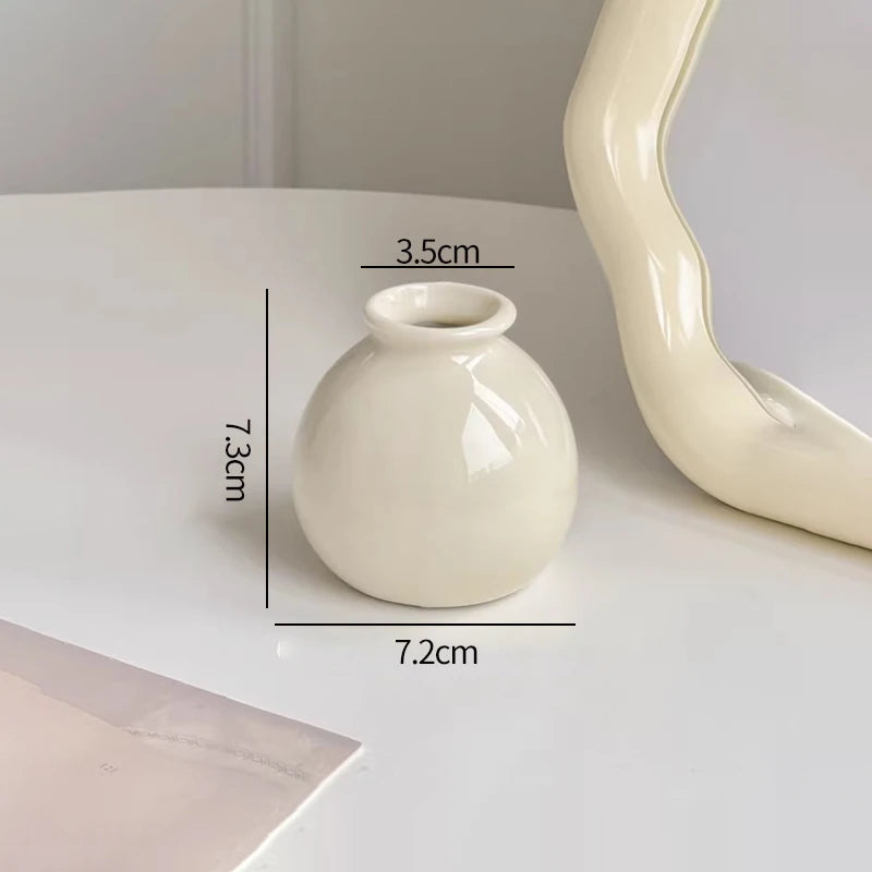 A white ceramic mini vase with a rounded body and narrow opening, shown on a white surface.