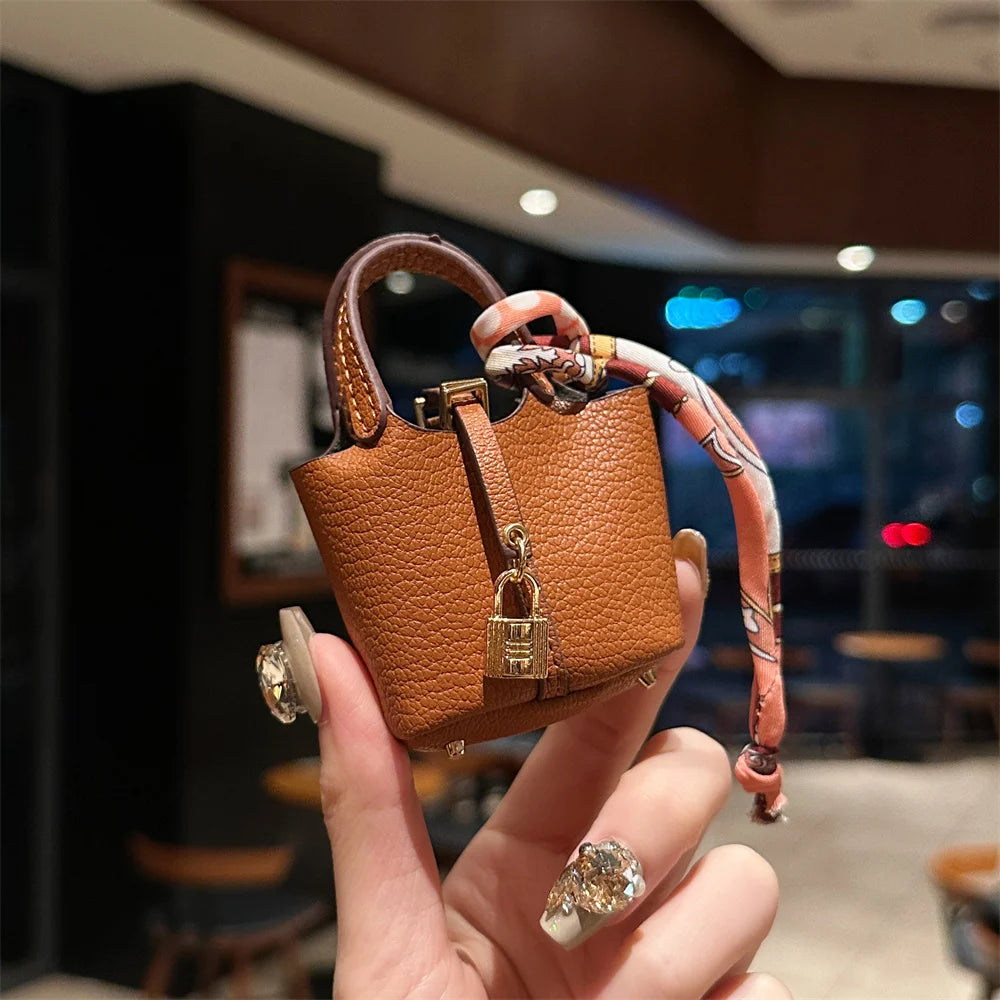 A hand holds a small brown leather handbag with a decorative wrist strap against a blurred indoor background.