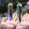 Two iridescent crystal pendants shaped like elongated prisms are held in a person's hand.