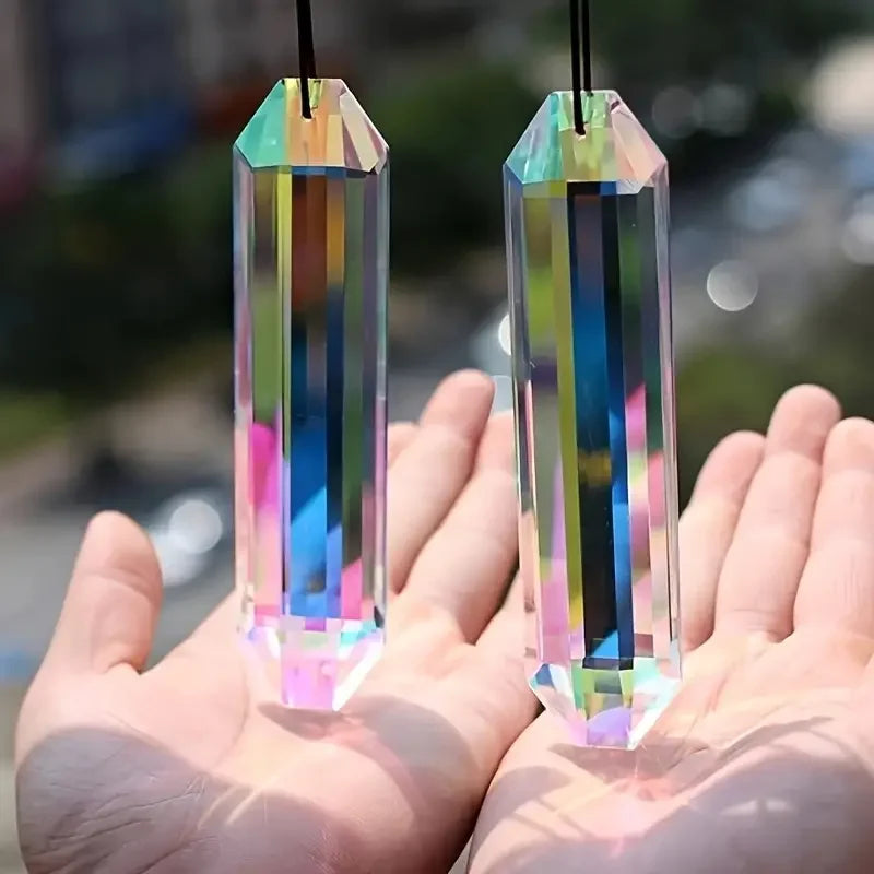 Two iridescent crystal pendants shaped like elongated prisms are held in a person's hand.