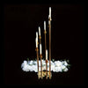 Elegant gold metal candle holders with white candles arranged above a bed of white flowers.
