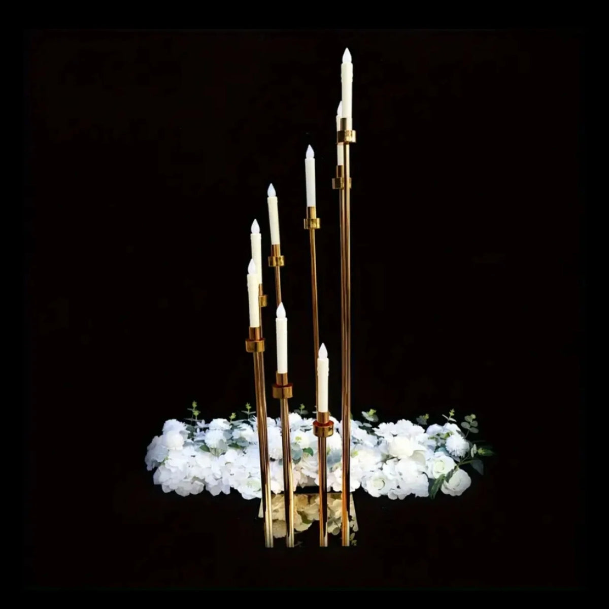 Elegant gold metal candle holders with white candles arranged above a bed of white flowers.