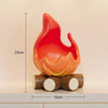 An orange-red resin fire spirit sculpture resting on two wooden logs.