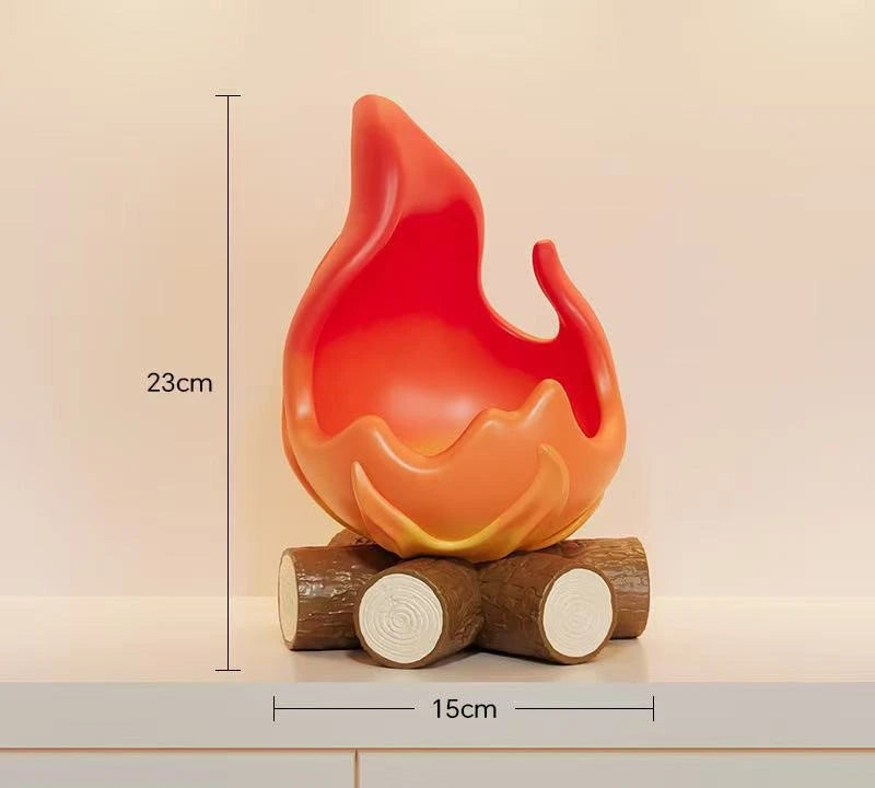 An orange-red resin fire spirit sculpture resting on two wooden logs.