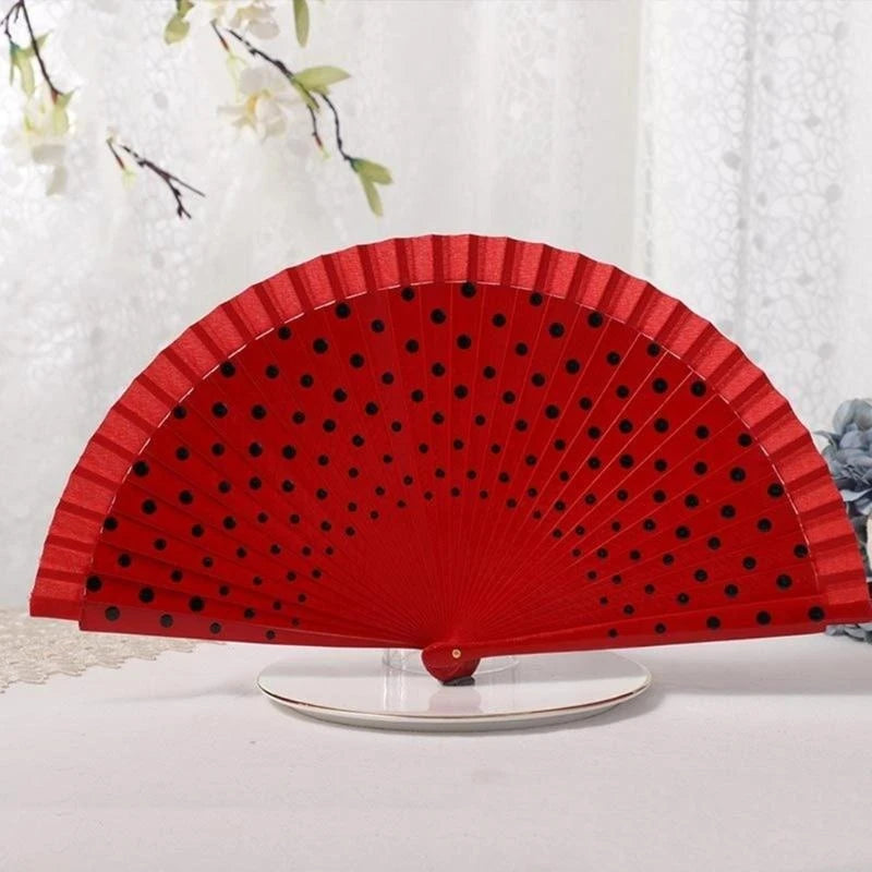 A bright red hand fan with black polka dots, displayed on a clear stand.