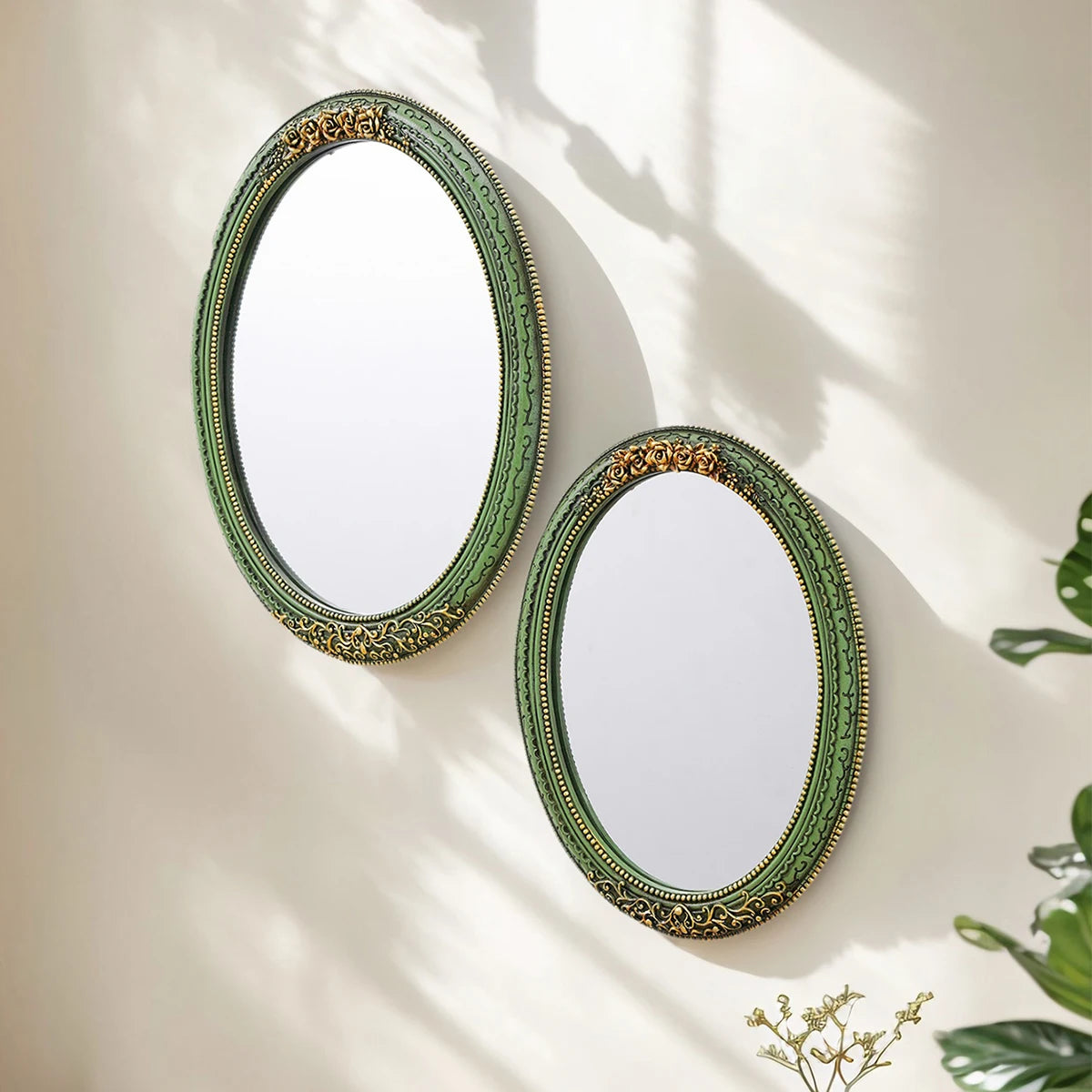 An oval wall mirror with a green frame featuring intricate gold lace design, casting shadows on a light wall.