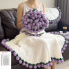 A woman is wearing a white knitted blanket with purple floral trim, sitting on a dark sofa.