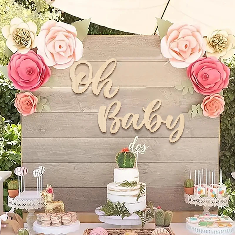 A wooden sign with 'Oh Baby' lettering surrounded by pink and cream roses, featuring a tiered cake and greenery for a baby sh