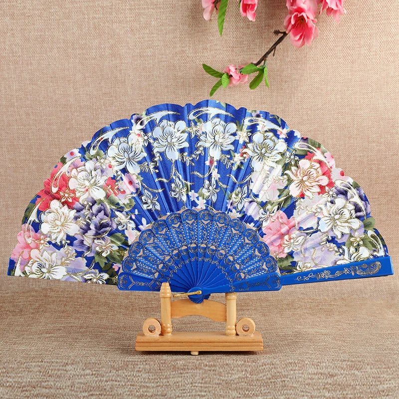 A blue and white floral silk folding fan displayed on a wooden stand.