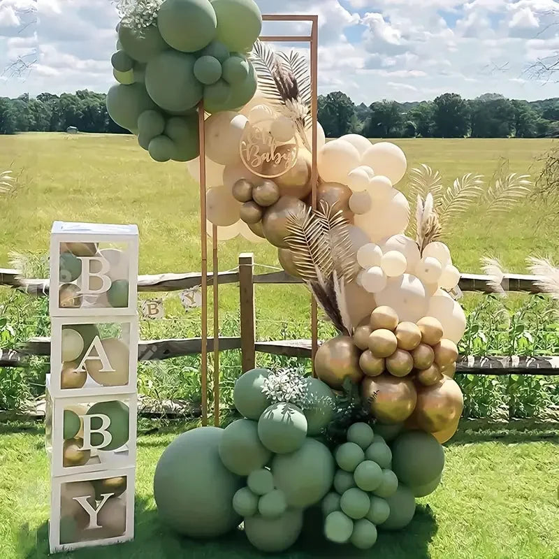 A large arrangement of pastel green and beige balloons is displayed outdoors in a grassy field.
