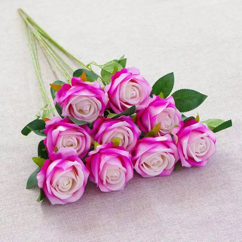 A bouquet of pink and purple velvet artificial roses with green leaves on a light fabric.