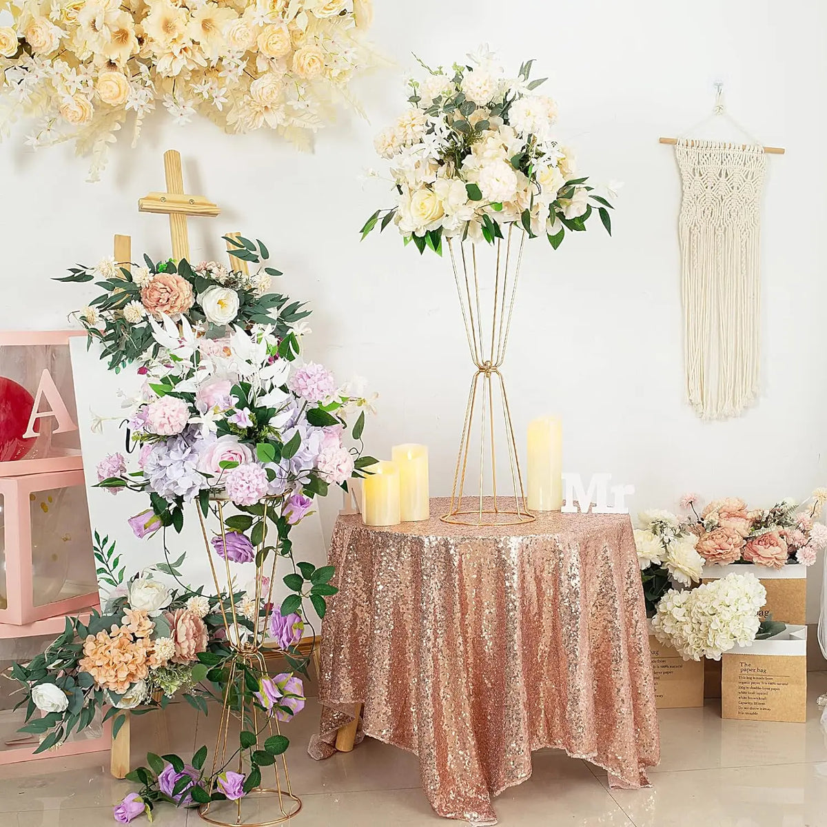 Gold geometric flower stands displaying white and pink floral arrangements on a draped table.