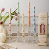 A collection of decorative printed long stick candles in various colors and floral patterns displayed on a light surface.