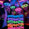 A display of various glow in the dark party glasses in multiple colors, held by people at a party.