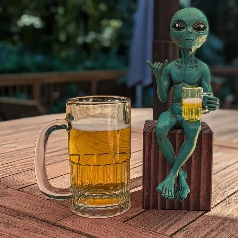 Resin green alien statue holding a glass of beer on a wooden table.