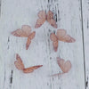 Several dried, pale pink organza butterfly embellishments are scattered on a white wooden surface.