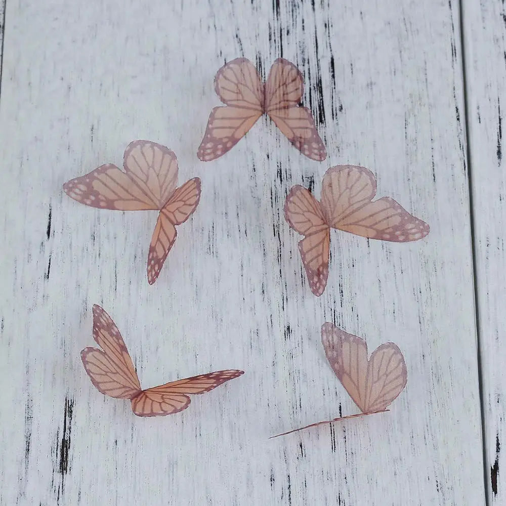Several dried, pale pink organza butterfly embellishments are scattered on a white wooden surface.