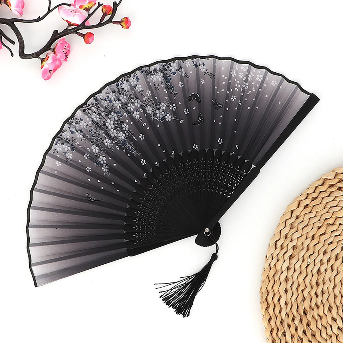 Black folding fan with sheer fabric and decorative elements next to a woven bamboo mat.