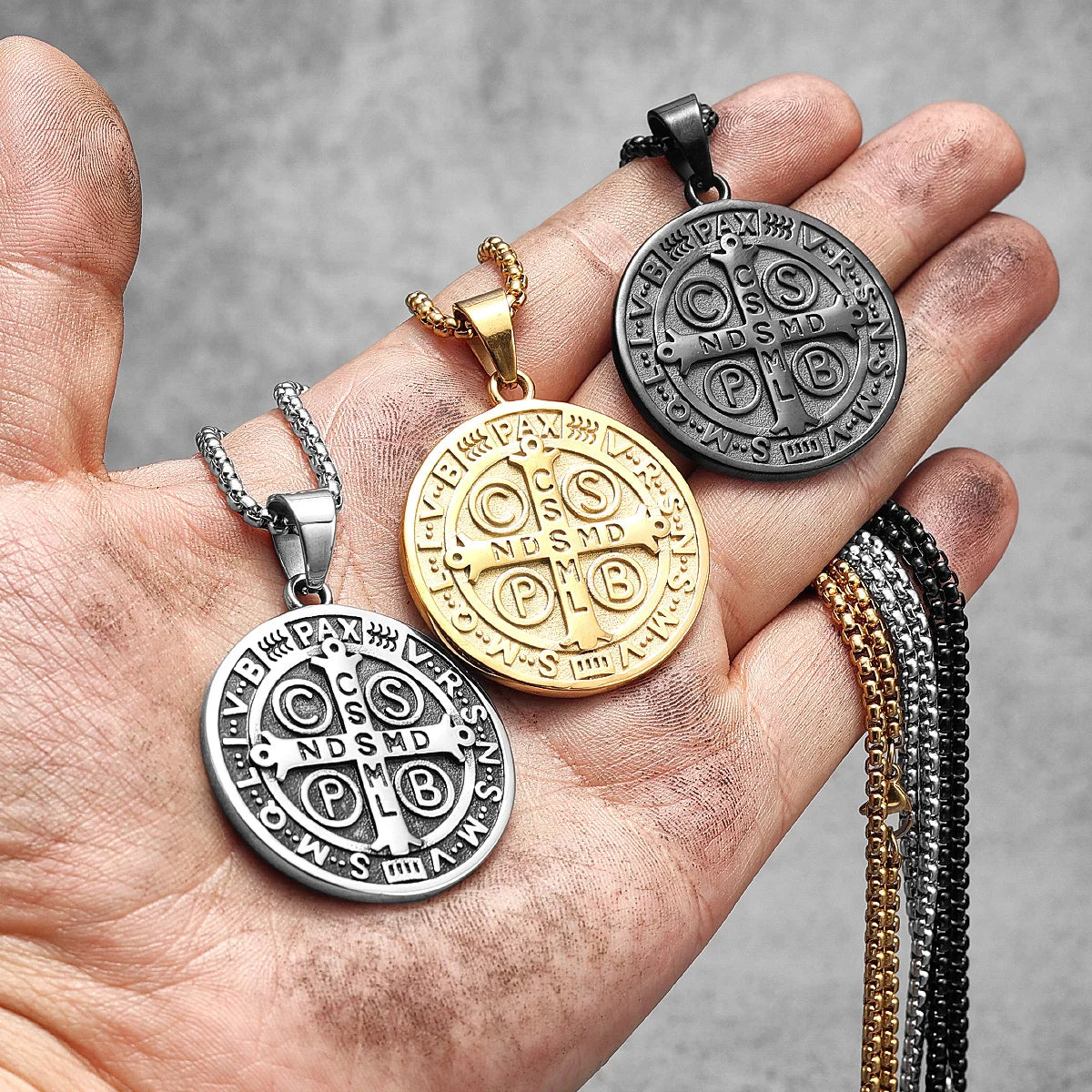 A hand holds three stainless steel punk cross necklaces featuring various symbols and designs.