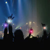 A hand raises an LED flash bracelet during a concert or performance, illuminated by stage lights.