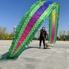Una persona realizando una danza de dragón con un gran atrezzo verde y morado colorido al aire libre.
