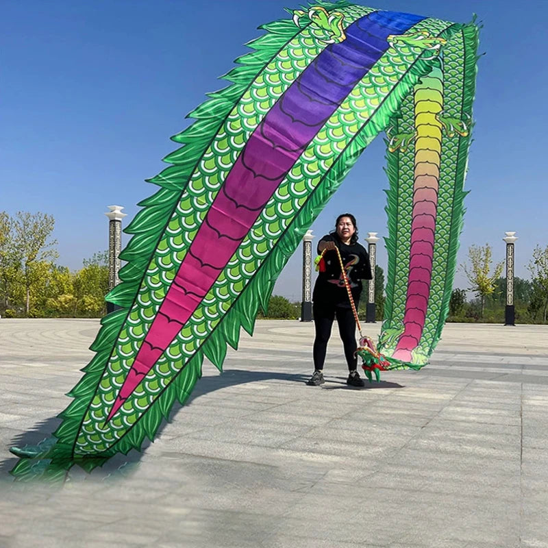 Una persona realizando una danza de dragón con un gran atrezzo verde y morado colorido al aire libre.