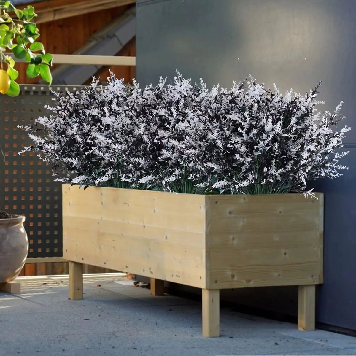 A wooden planter filled with artificial lavender stems covered in white frost-like material, set against a gray wall.