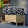 A wooden planter filled with artificial lavender stems covered in white frost-like material, set against a gray wall.