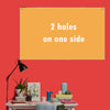 A bright orange rectangular sign with the text 2 holes on one side displayed on a red wall.