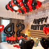 A balloon garland decoration featuring red and black foil number balloons above a birthday cake.