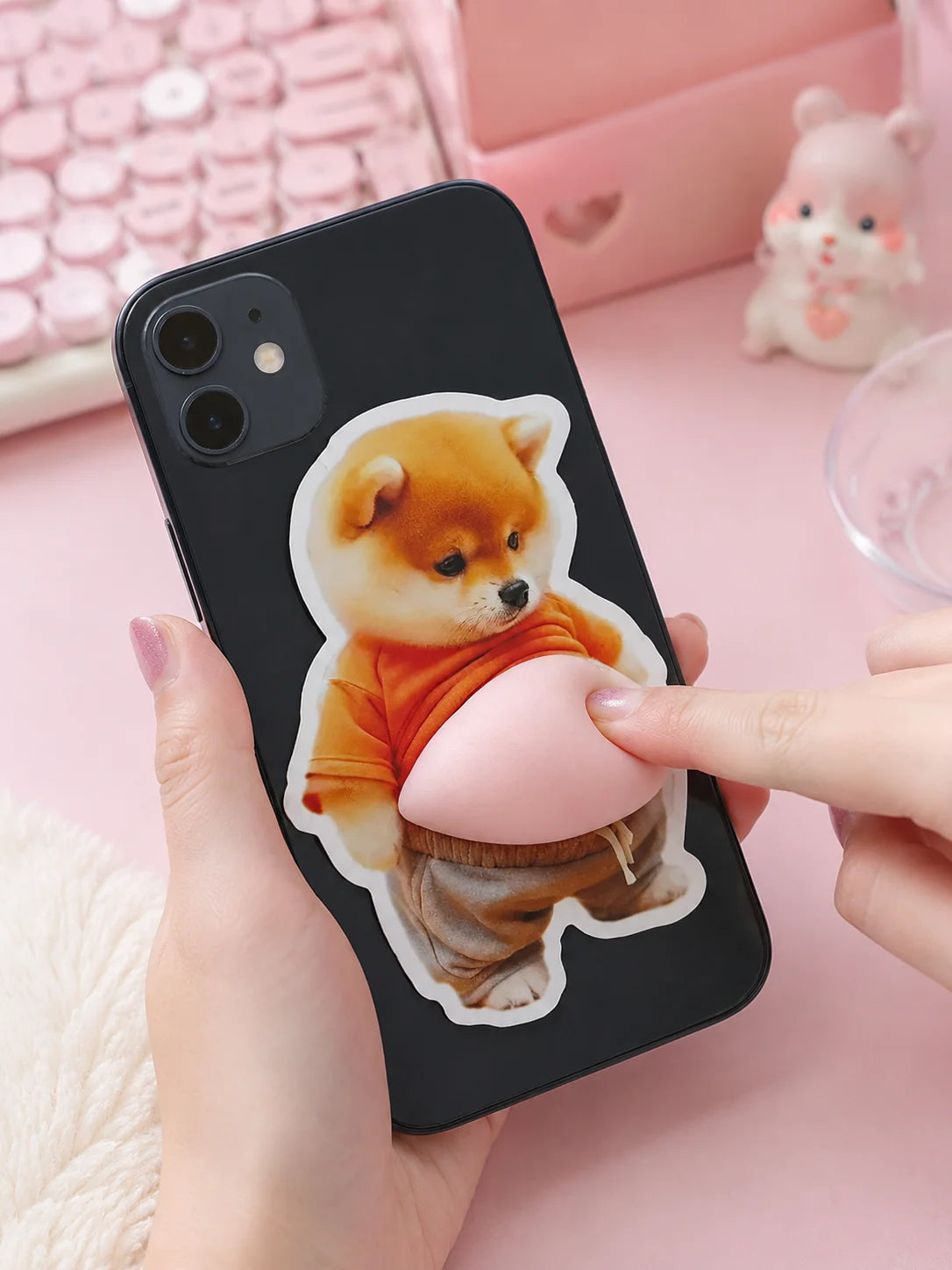 A hand holds a black smartphone displaying a soft pink 3D Shiba Inu squishy sticker decal.