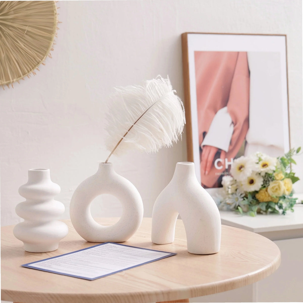 A set of white ceramic vases and a feather decoration displayed on a wooden table.