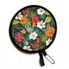 A circular, black handheld fan with a floral pattern featuring orange, red, and white flowers on green leaves.
