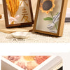 A wooden photo frame displaying dried flowers, including yellow and orange blooms, set against a light background.