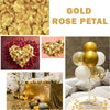 Gold rose petals and gold balloons arranged on a table with greenery.
