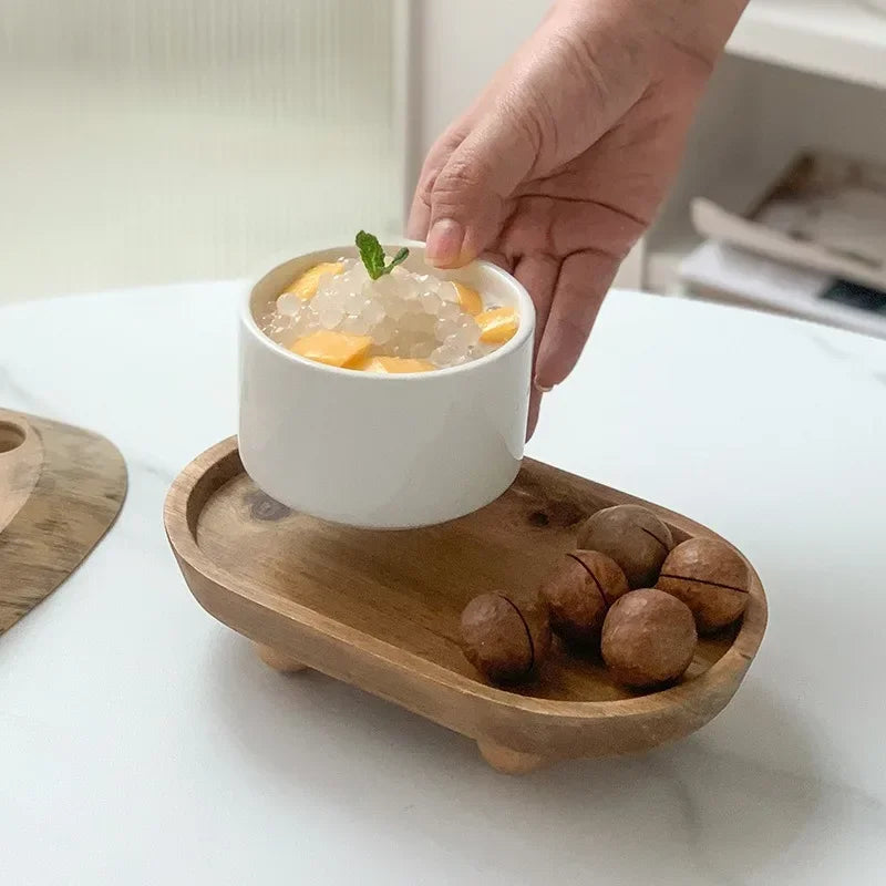 A hand is holding a white bowl filled with ice and fruit on a wooden tray.