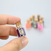 A hand holds a small glass bottle of purple glitter powder for party decorations next to several other similar bottles.