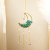 A handcrafted gold moon crystal suncatcher with a turquoise pendant and prism charms hanging against a light background.