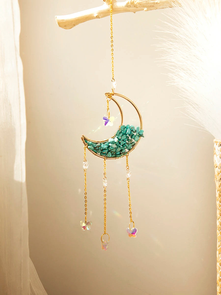 A handcrafted gold moon crystal suncatcher with a turquoise pendant and prism charms hanging against a light background.