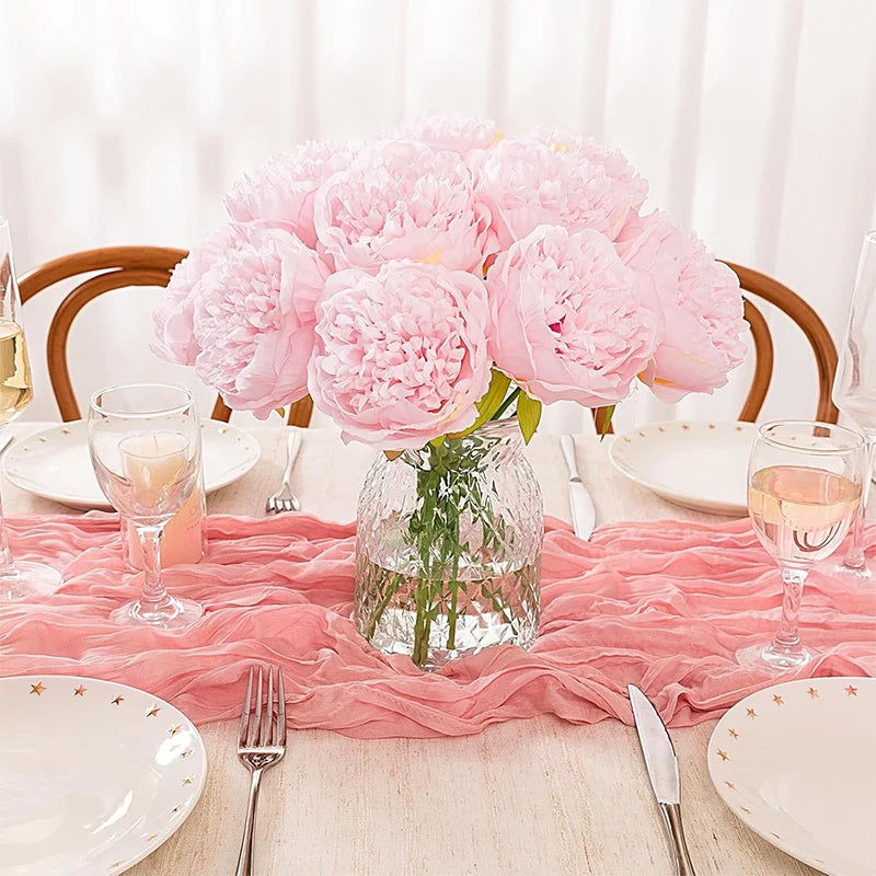 A centerpiece of pink silk peony artificial flowers in a glass vase on a wooden table setting.