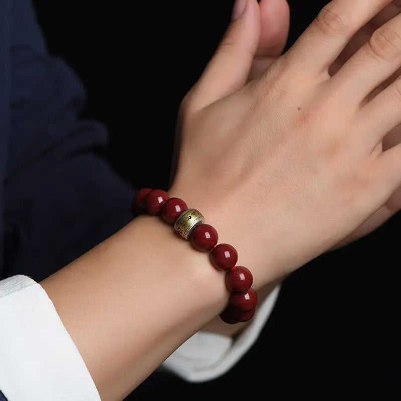A close-up of a hand wearing a bracelet made of smooth, reddish-brown cinnabar stones.