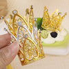 Gold and silver mini crown cake toppers and decorations displayed on a light green plate.