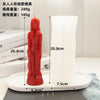 A red silicone mold of a realistic human figure stands next to a white pillar candle on a white tray.