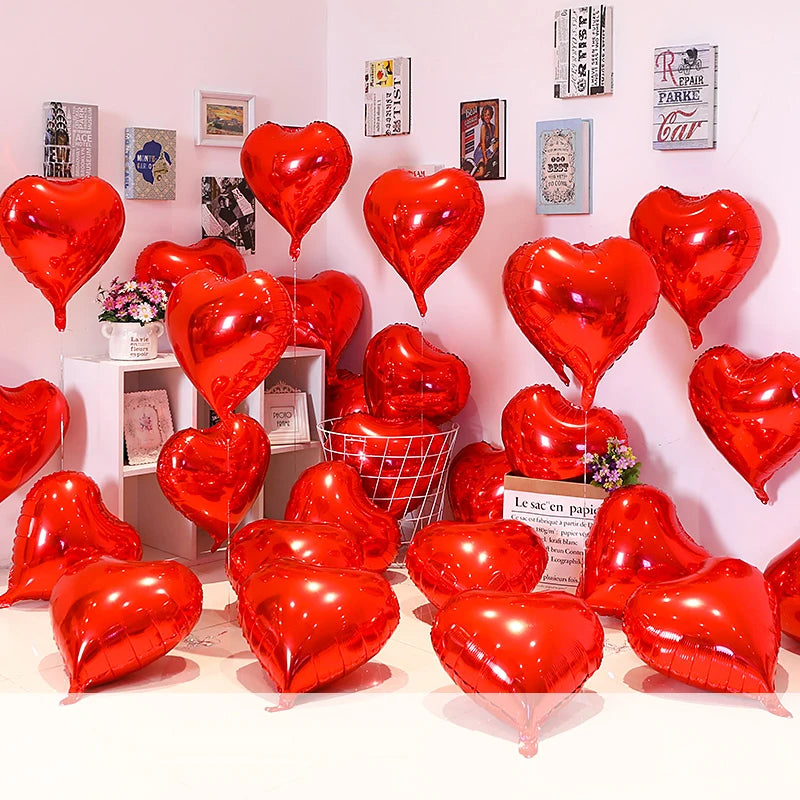 A collection of red heart foil balloons displayed against a white wall.