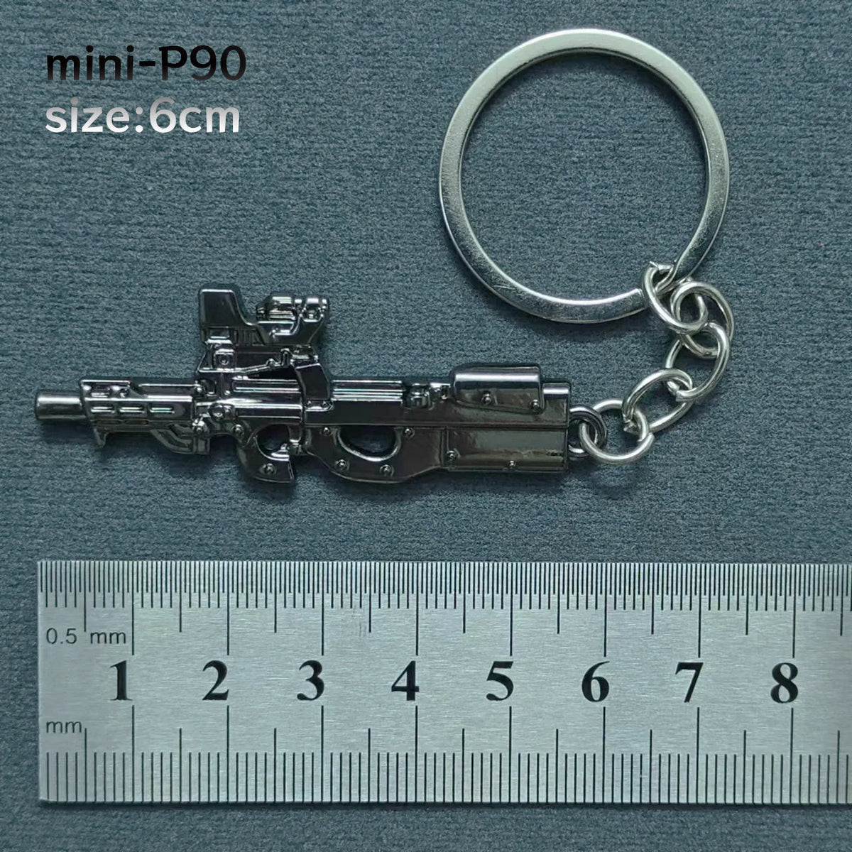 A silver miniature replica of an alloy gun model attached to a keyring, measured against a ruler.