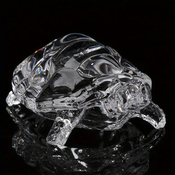 Un ornamento de tortuga de cristal transparente reflejándose en una superficie oscura.