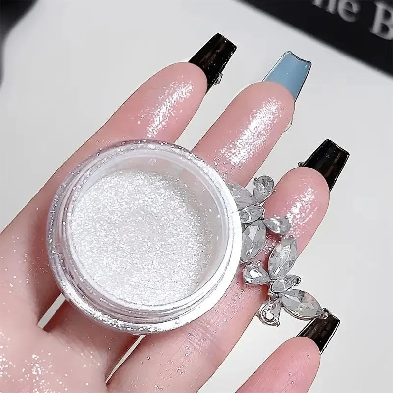A hand holds a jar of white glitter body highlight powder and a silver crystal bracelet.