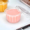 A clear disposable dessert cup with a lid filled with pink liquid sits on a white surface.