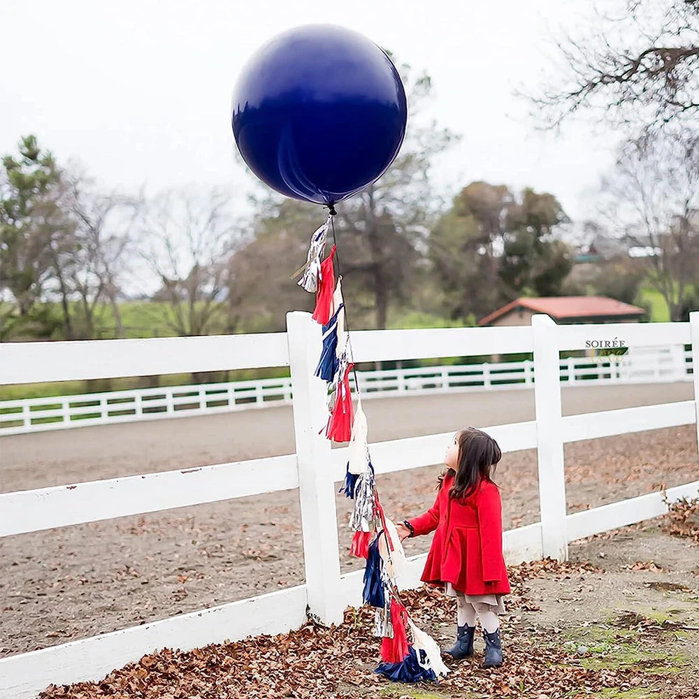 A girl stands in front of a white fence with a navy blue balloon floating above.